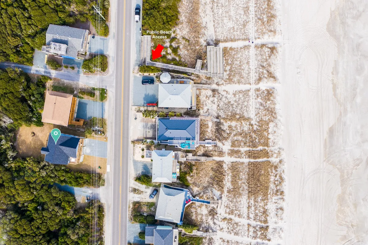 A welcoming public beach access point set among residential homes, with a road leading directly to the sandy shore. The scene encourages the idea of spontaneous beach outings and easy strolls from home to water.