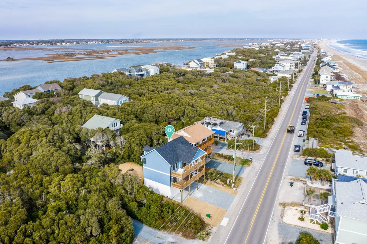This image features a house with a striking blue exterior nestled among lush greenery, with a coastal road and a nearby water body visible. The setting is welcoming and hints at easy access to local attractions, beach outings, and nearby restaurants.