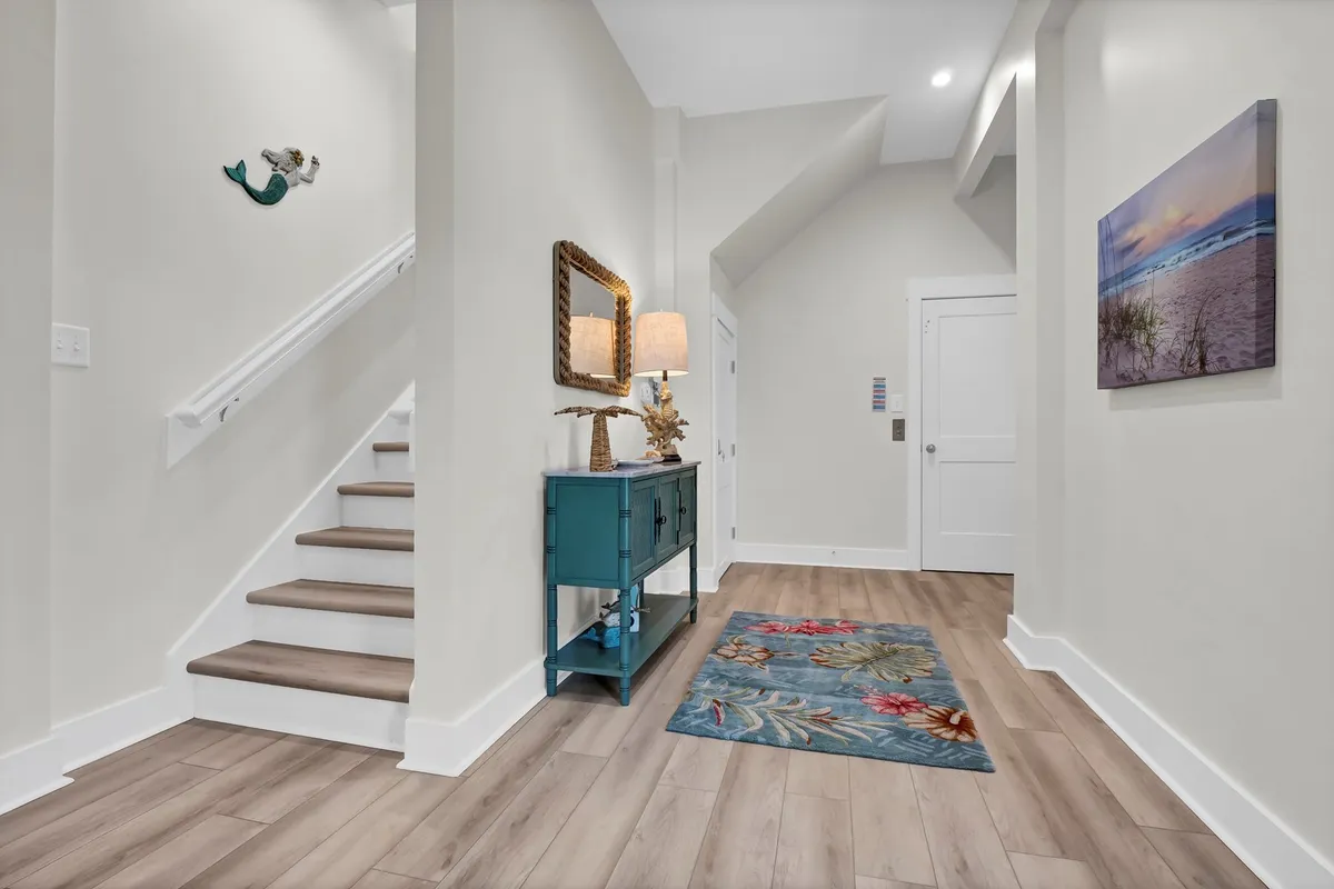 A welcoming entryway with a stylish staircase, a decorative console table topped with a mirror, and tasteful wall art. The area rug and soft lighting create a cozy, inviting first impression.