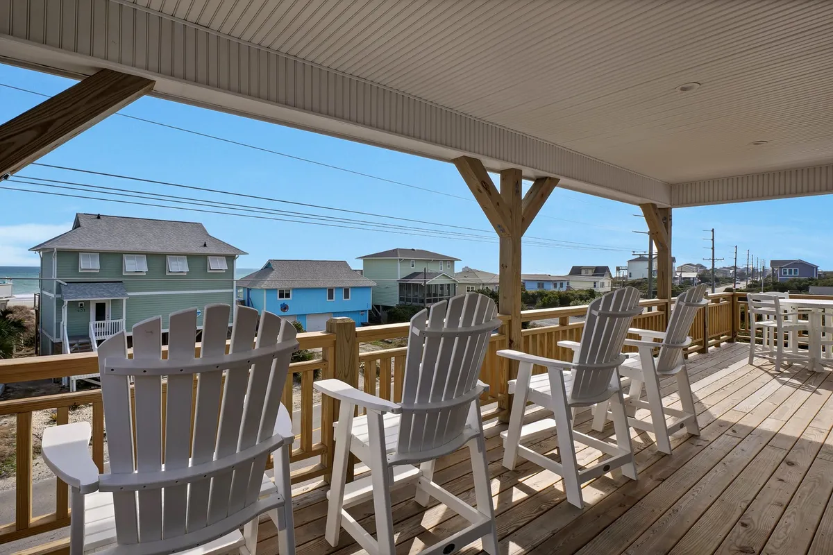 A tranquil exterior scene featuring adirondack chairs positioned to take in ocean views, with colorful beach houses in the background. This spot is ideal for relaxing, socializing, and enjoying the scenic coastal atmosphere that Topsail Beach is known for.