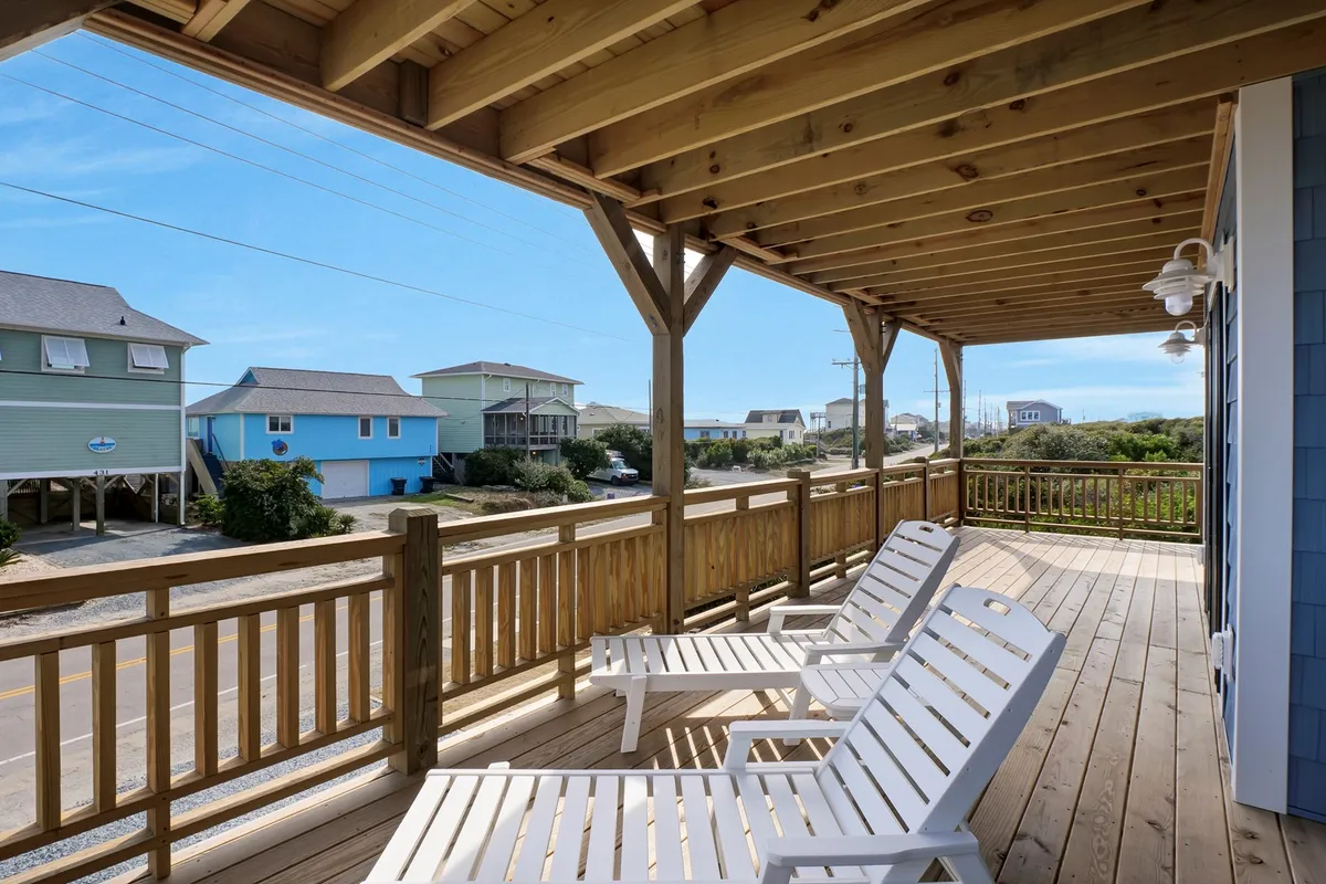 A wooden deck furnished with lounge chairs directly faces the ocean, offering an uninterrupted view of the waves. The space is bathed in natural light, emphasizing its role as a serene spot for relaxation and connection to the coastal environment.