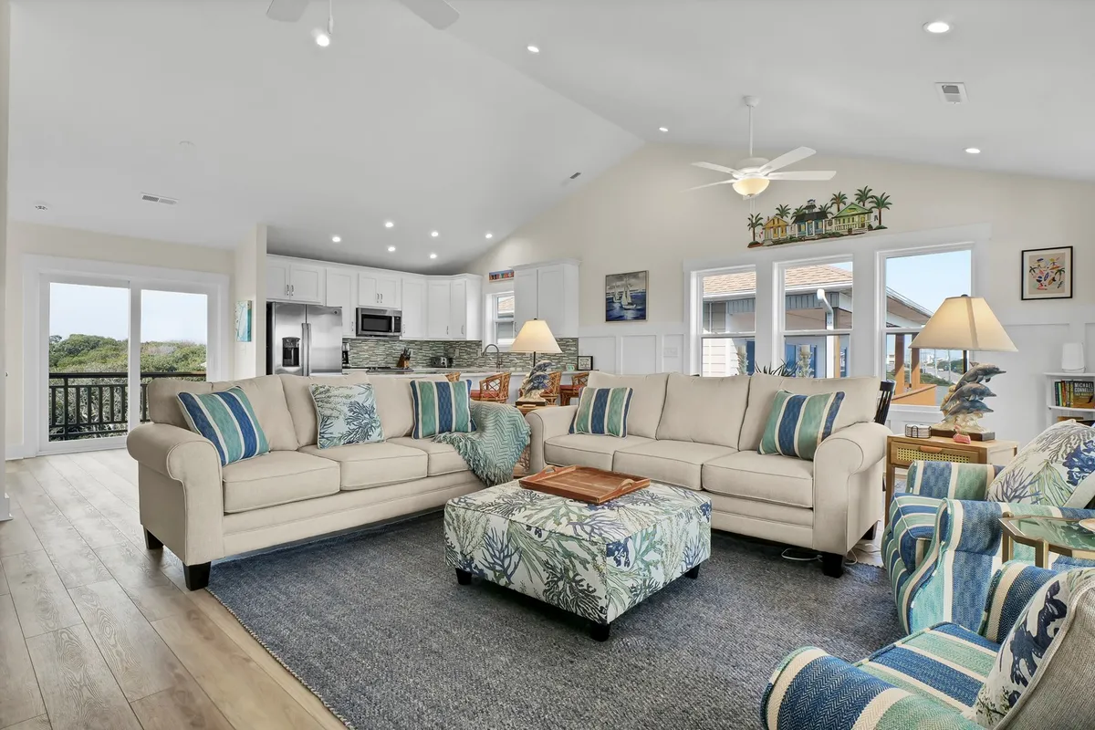 This image depicts a welcoming living area with comfortable sofas, colorful accent chairs, a decorative ottoman, and large windows offering scenic views. The arrangement is ideal for group gatherings, game nights, or morning coffee with friends.