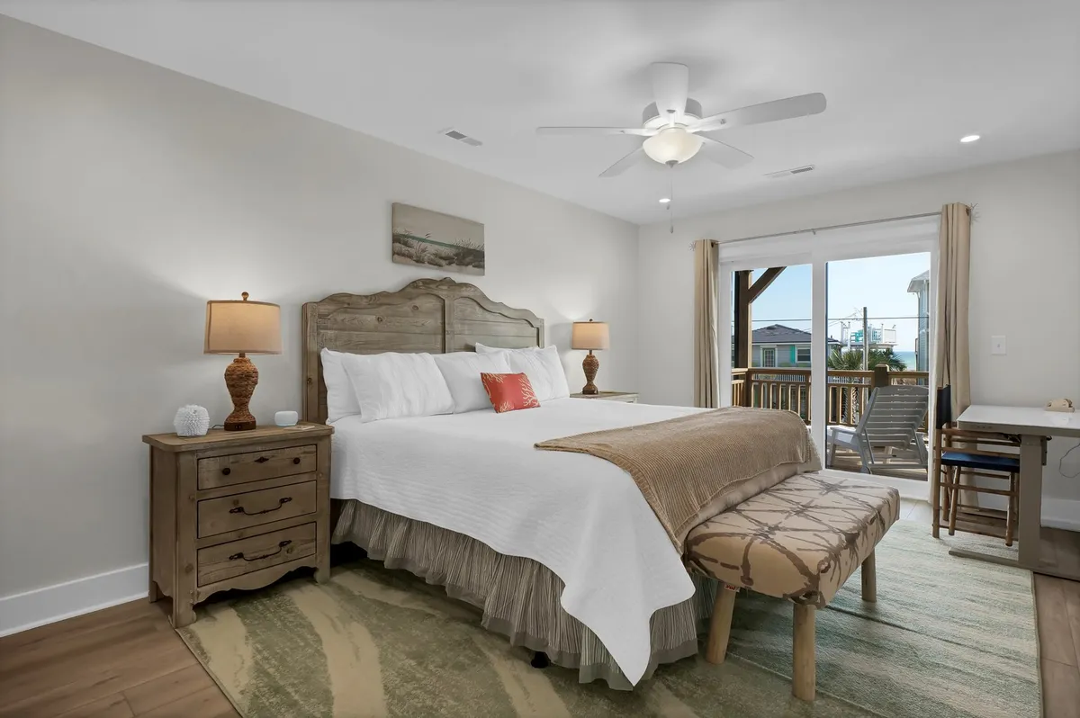 A calm, sunlit bedroom featuring a large bed with plush bedding, a decorative bench at the foot, matching nightstands with soft lighting, and a window offering serene morning views.