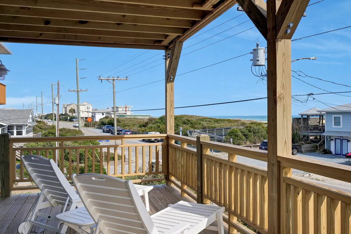 A stylish wooden deck with white lounge chairs overlooks the ocean, creating a bright and inviting space ideal for socializing or quiet moments. The horizon and waves are clearly visible, and the arrangement encourages both relaxation and interaction.