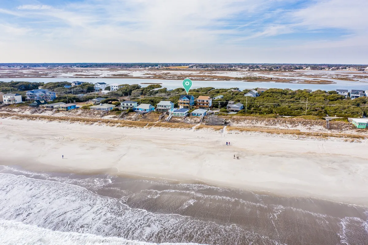 A tranquil beach scene with sandy shoreline, gentle ocean waves, and beachfront houses framed by coastal vegetation. The image evokes the feeling of a relaxing, fun-filled day at the beach, perfect for families seeking outdoor adventure and seaside play.