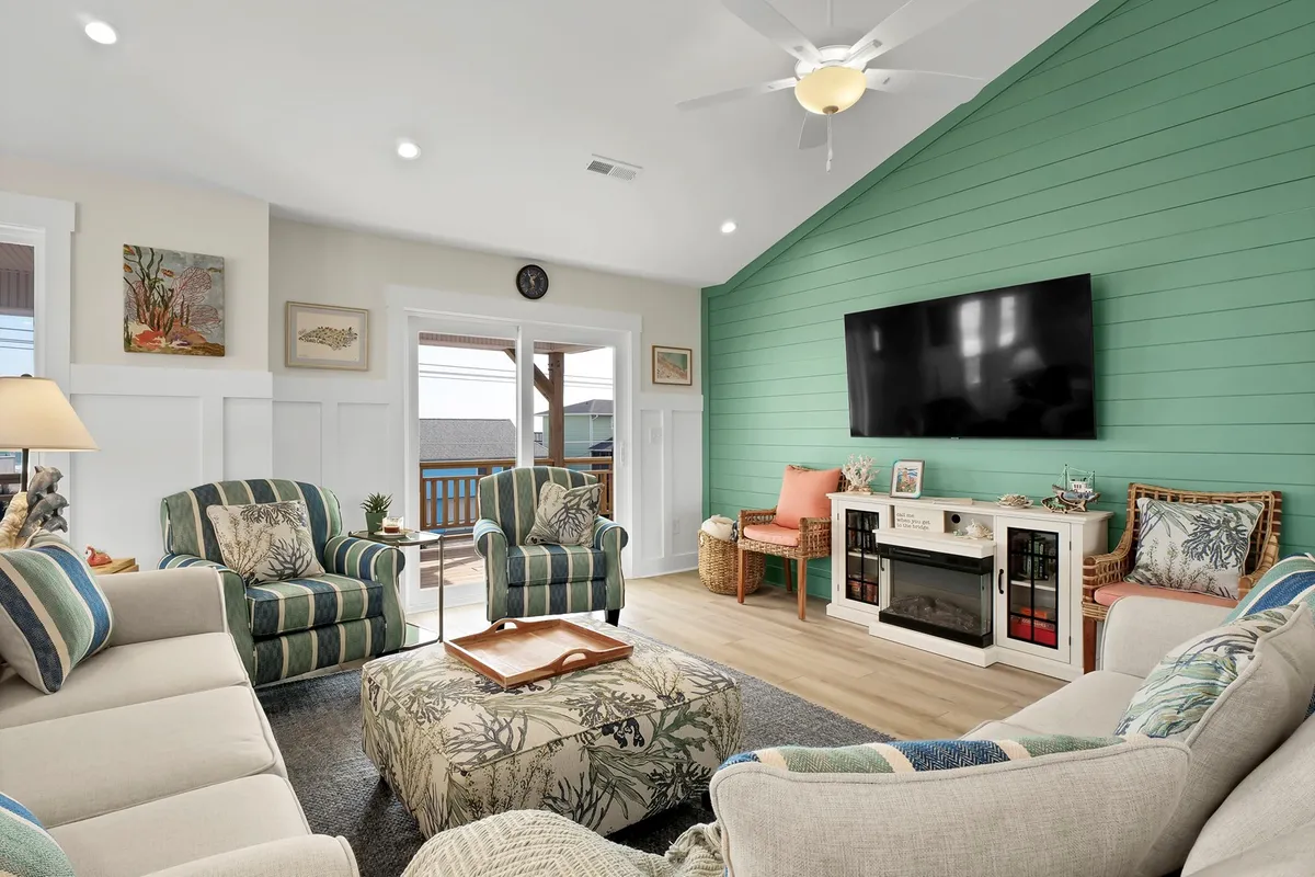 A welcoming living space featuring comfortable seating, a green accent wall, a television, and decorative touches. Large windows suggest access to lovely views and a bright, airy atmosphere—perfect for unwinding, movie nights, or board games.