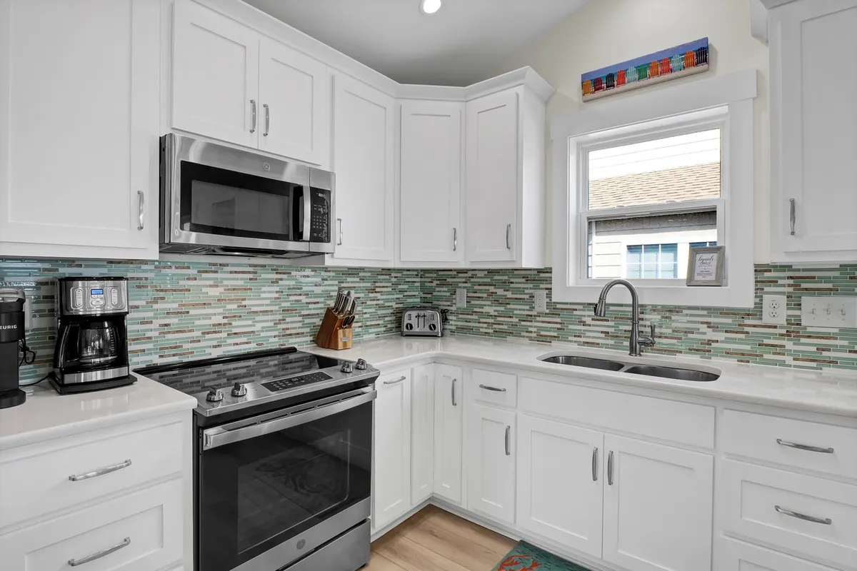 A bright, modern kitchen with stainless steel appliances, a colorful backsplash, crisp white cabinetry, and a window above the sink. The space feels cheerful and inviting—ideal for preparing meals and gathering around for casual conversation.