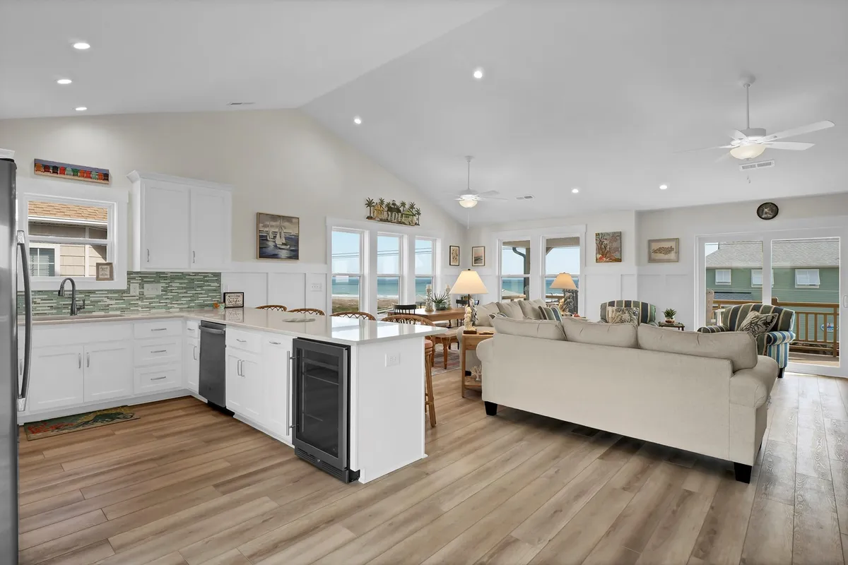 This image features a stunning open-concept main social area, with a spacious living room, comfortable seating, a kitchen island, a dining area, and large windows flooding the space with natural light and offering lovely views. The design seamlessly connects cooking, dining, and relaxing spaces.