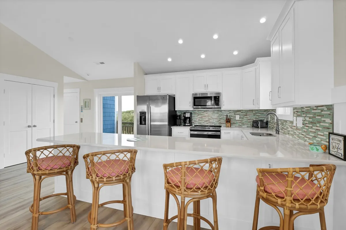 The image showcases a modern kitchen with a large island, bar stools, elegant cabinetry, backsplash, and stainless appliances. The setup is ideal for collaborative cooking or sharing drinks before a night out.