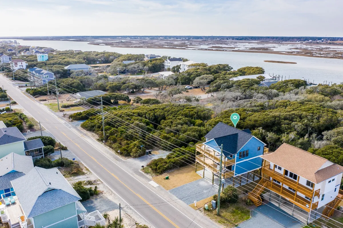 A wide view of the coastline featuring modern homes set against lush greenery, with the sparkling water visible in the background. The scene invites exploration and relaxation, emphasizing connection to both nature and the local community.